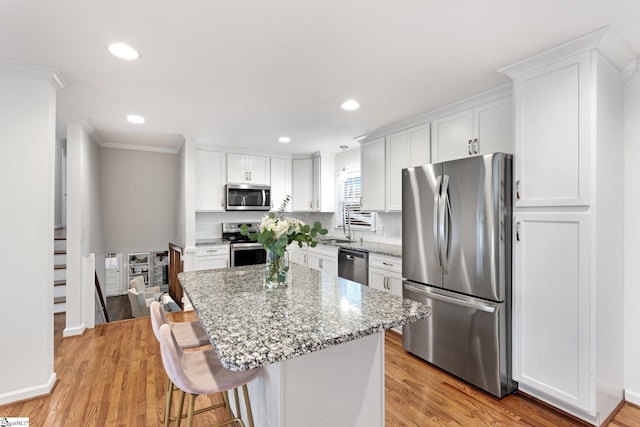 kitchen with a kitchen breakfast bar, appliances with stainless steel finishes, white cabinets, light stone countertops, and a kitchen island