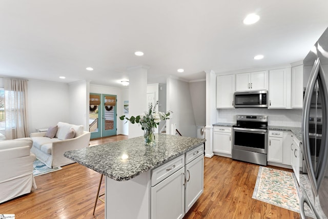 kitchen featuring white cabinets, appliances with stainless steel finishes, a kitchen island, dark stone countertops, and decorative backsplash