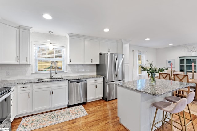 kitchen with sink, stainless steel appliances, white cabinets, and decorative light fixtures