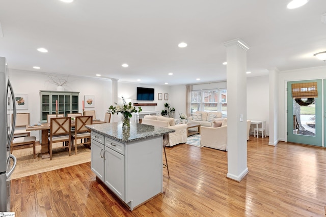 kitchen with decorative columns, white cabinets, a kitchen island, dark stone countertops, and light wood-type flooring