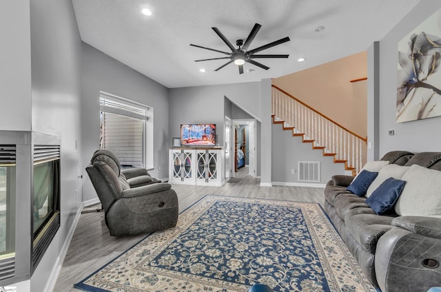 living room featuring light wood-type flooring, ceiling fan, a multi sided fireplace, and a textured ceiling