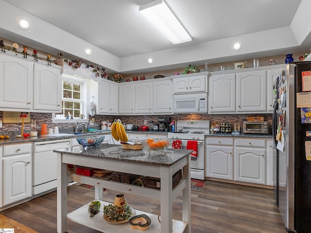 kitchen with white appliances, white cabinetry, decorative backsplash, dark stone countertops, and dark wood-type flooring