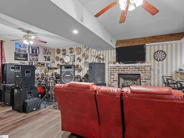 living room featuring a fireplace, light hardwood / wood-style floors, a textured ceiling, and ceiling fan