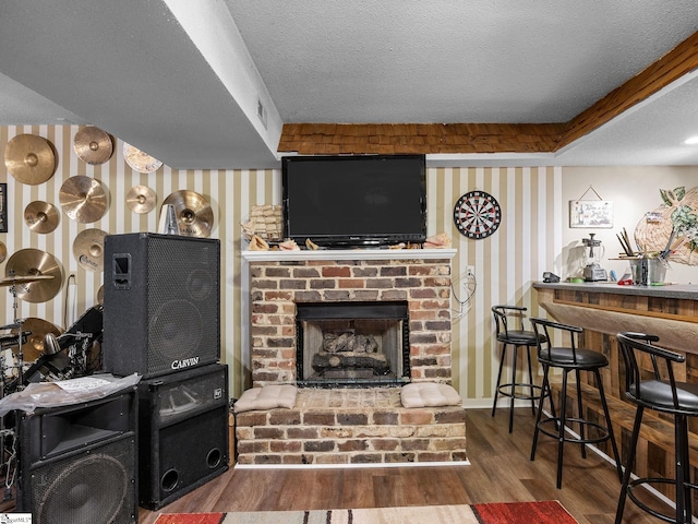 living room with hardwood / wood-style flooring, a brick fireplace, a textured ceiling, and bar area