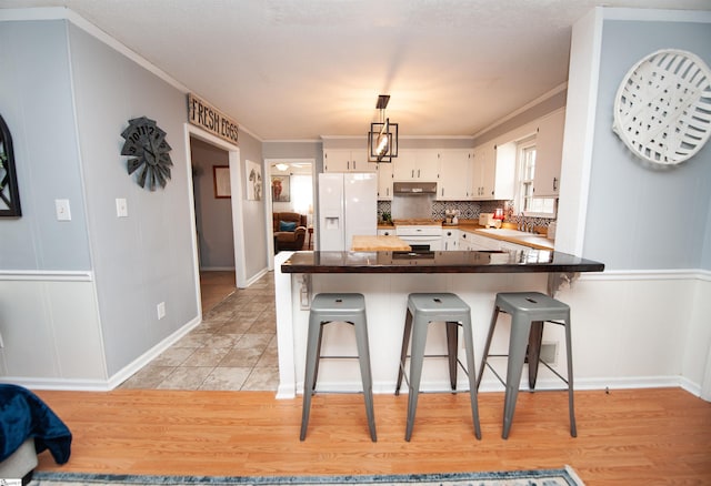 kitchen with kitchen peninsula, white refrigerator with ice dispenser, white cabinetry, stove, and a kitchen bar