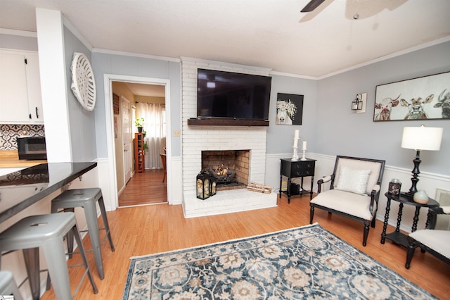 living room featuring crown molding, light hardwood / wood-style flooring, a fireplace, and ceiling fan