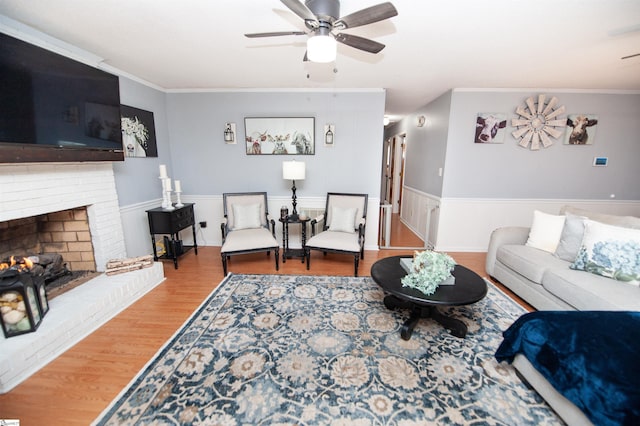 living room with crown molding, light hardwood / wood-style floors, ceiling fan, and a brick fireplace