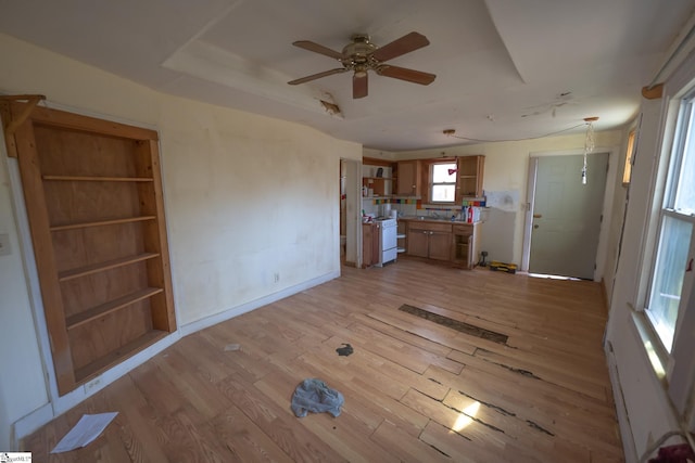 unfurnished living room with ceiling fan, light hardwood / wood-style floors, and a tray ceiling