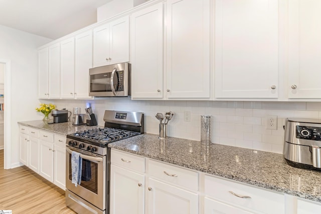 kitchen featuring appliances with stainless steel finishes, white cabinetry, backsplash, light stone countertops, and light wood-type flooring