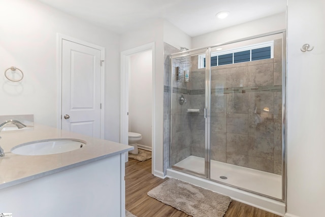 bathroom featuring wood-type flooring, toilet, a shower with door, and vanity