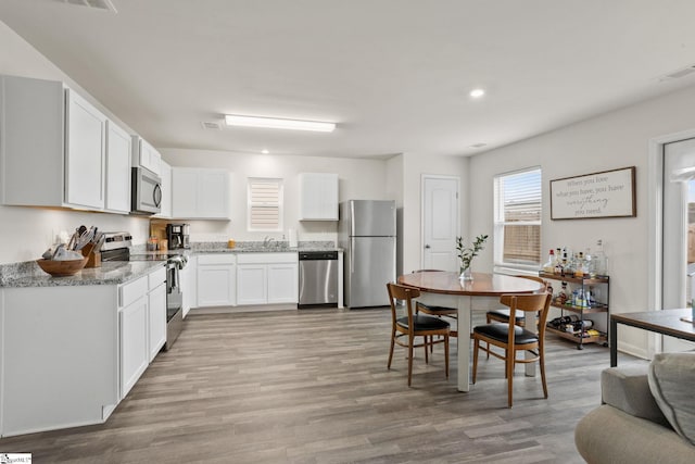 kitchen featuring sink, white cabinetry, light stone counters, wood-type flooring, and appliances with stainless steel finishes