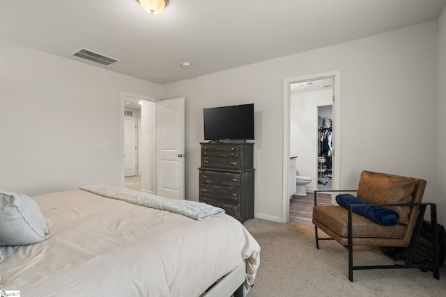 bedroom with ensuite bath, a walk in closet, light colored carpet, and a closet