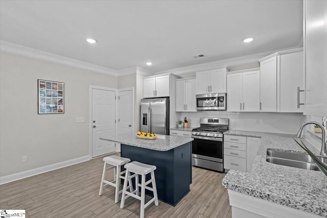 kitchen with sink, appliances with stainless steel finishes, white cabinetry, a center island, and light stone counters