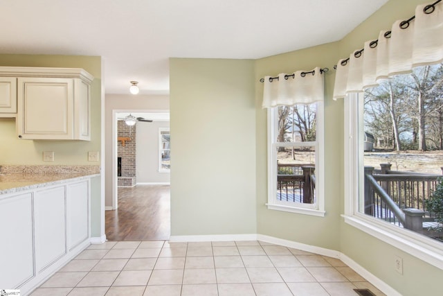 kitchen featuring light stone counters, a brick fireplace, light tile patterned floors, ceiling fan, and cream cabinetry