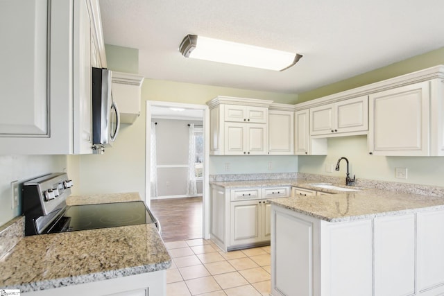 kitchen featuring sink, light tile patterned floors, appliances with stainless steel finishes, white cabinetry, and kitchen peninsula