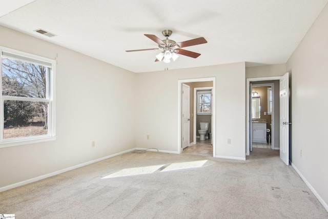 unfurnished bedroom with multiple windows, ensuite bathroom, light colored carpet, and ceiling fan