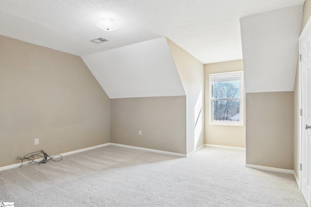 additional living space with light colored carpet, vaulted ceiling, and a textured ceiling