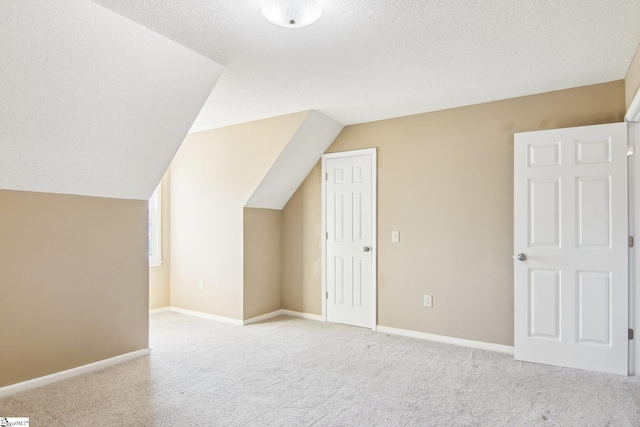 bonus room featuring vaulted ceiling, light colored carpet, and a textured ceiling