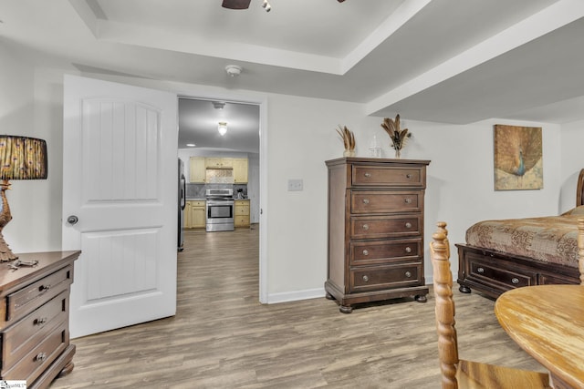 bedroom with a tray ceiling, stainless steel fridge, ceiling fan, and light wood-type flooring