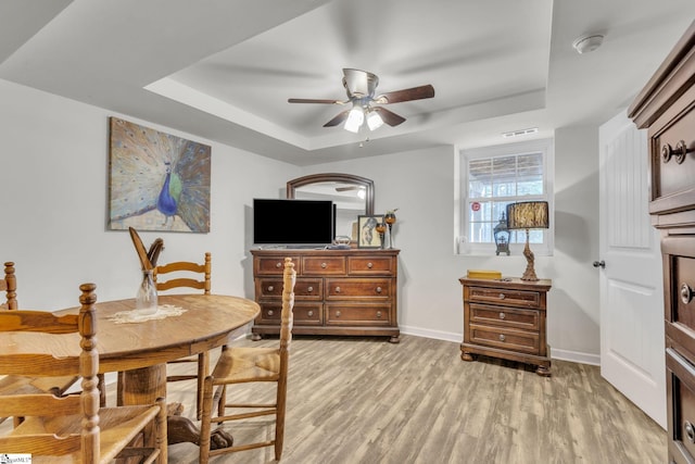 dining space featuring ceiling fan, a tray ceiling, and light wood-type flooring