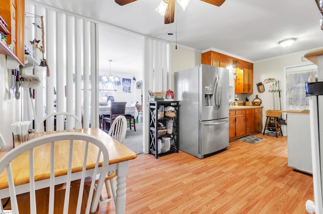 kitchen featuring stainless steel refrigerator with ice dispenser, ornamental molding, ceiling fan with notable chandelier, and light wood-type flooring