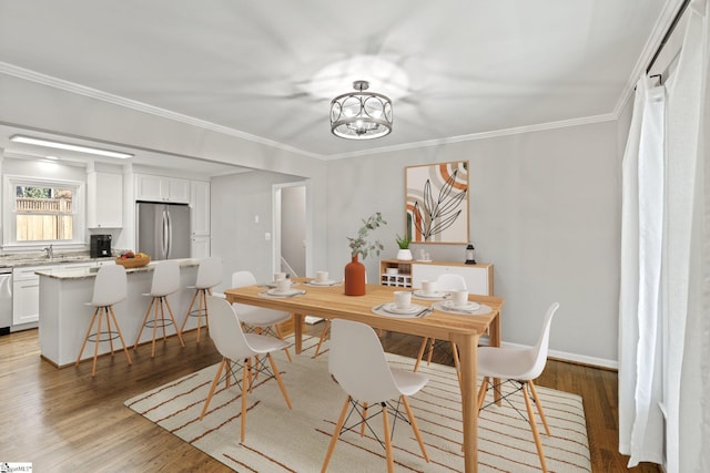 dining space with hardwood / wood-style floors, ornamental molding, sink, and a chandelier