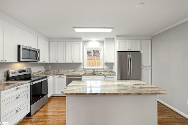 kitchen with sink, a kitchen island, stainless steel appliances, light stone countertops, and white cabinets