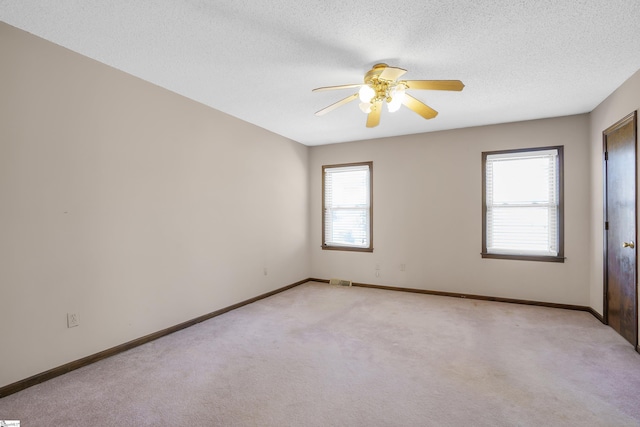 carpeted spare room with ceiling fan, a textured ceiling, and a wealth of natural light