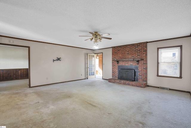 unfurnished living room featuring light colored carpet, a textured ceiling, ornamental molding, ceiling fan, and a fireplace