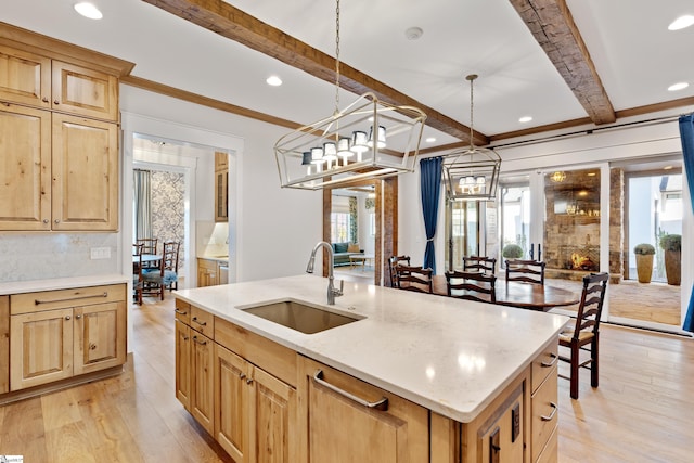 kitchen with sink, hanging light fixtures, an island with sink, beamed ceiling, and light hardwood / wood-style floors