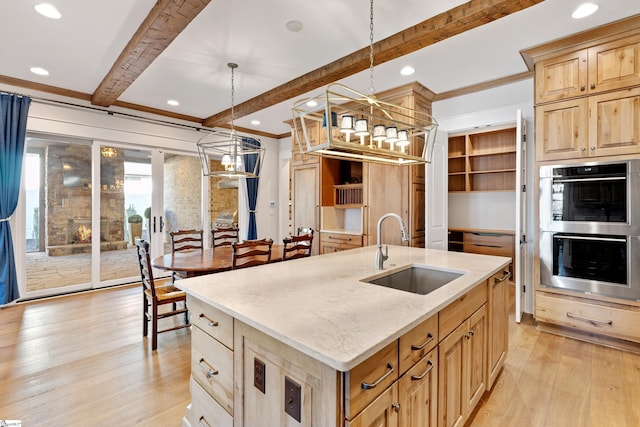 kitchen with pendant lighting, beam ceiling, a kitchen island with sink, and sink