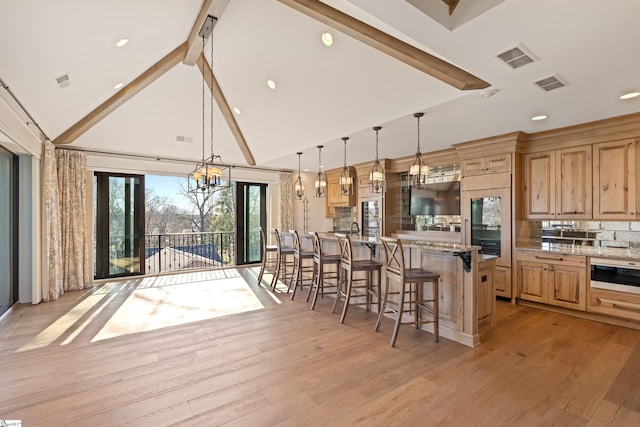 kitchen with light stone counters, high vaulted ceiling, a breakfast bar area, and pendant lighting