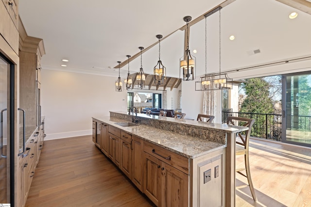 kitchen with a breakfast bar, sink, light stone counters, decorative light fixtures, and light hardwood / wood-style floors