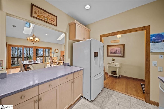 kitchen featuring a skylight, hanging light fixtures, light brown cabinets, a notable chandelier, and white refrigerator with ice dispenser