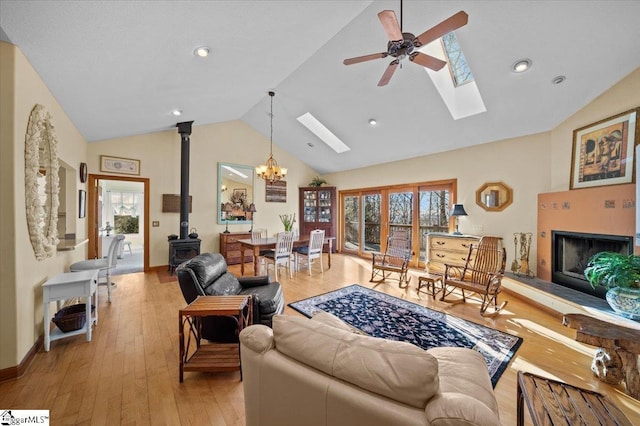 living room featuring a healthy amount of sunlight, ceiling fan with notable chandelier, light hardwood / wood-style flooring, and a wood stove