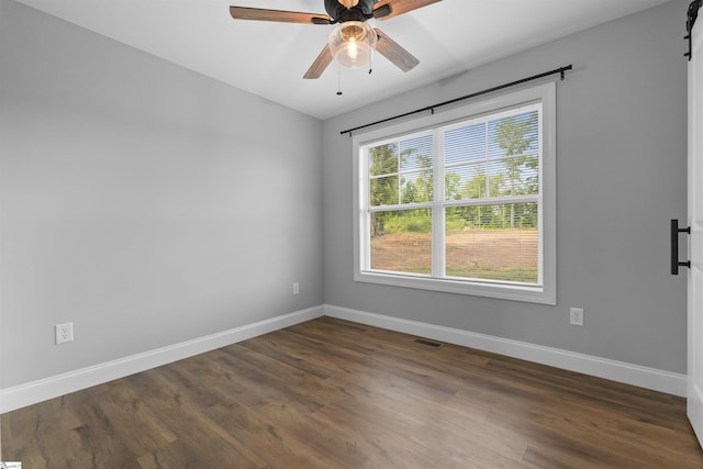 spare room with a barn door, dark wood-type flooring, and ceiling fan