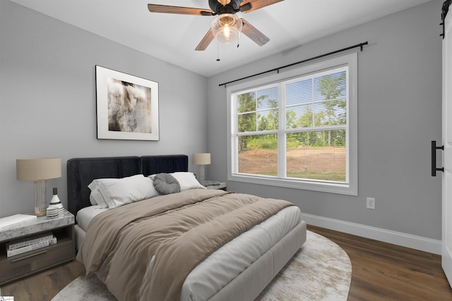 bedroom featuring dark wood-type flooring, a barn door, and ceiling fan