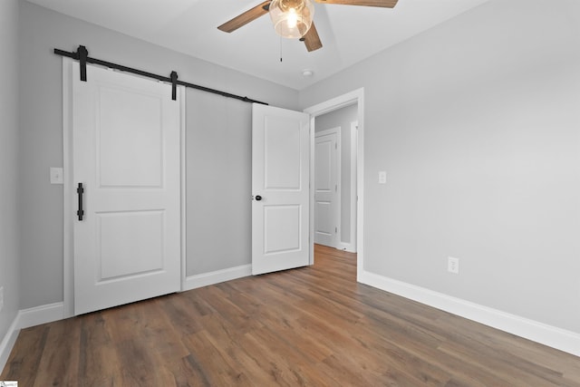 unfurnished bedroom featuring a barn door, hardwood / wood-style floors, ceiling fan, and a closet