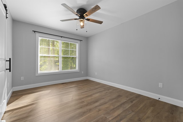 empty room featuring wood-type flooring, a barn door, and ceiling fan