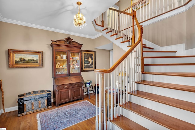 staircase with hardwood / wood-style flooring, ornamental molding, and a notable chandelier