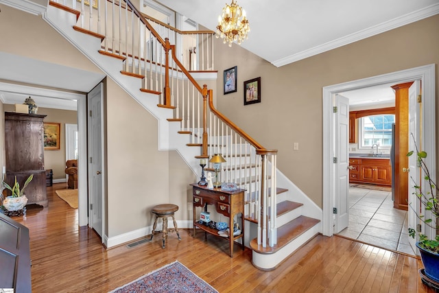 staircase featuring sink, ornamental molding, hardwood / wood-style floors, and a chandelier