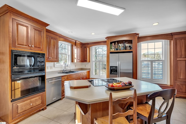 kitchen with sink, a breakfast bar area, a center island, black appliances, and light tile patterned flooring