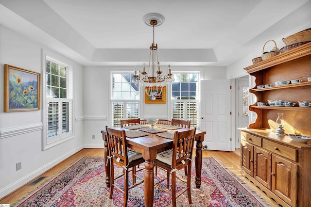 dining room featuring an inviting chandelier, a tray ceiling, and light hardwood / wood-style flooring