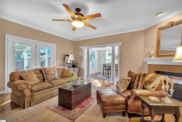 living room featuring ornate columns, crown molding, light wood-type flooring, ceiling fan, and a fireplace