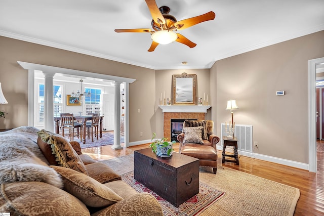 living room featuring ceiling fan with notable chandelier, hardwood / wood-style floors, decorative columns, a tiled fireplace, and ornamental molding