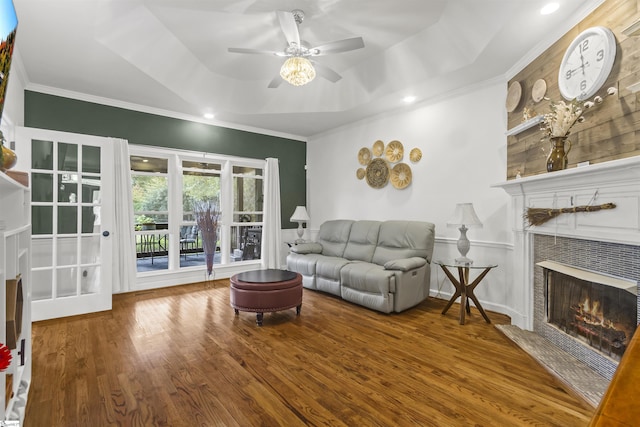 living room with wood-type flooring, ornamental molding, a raised ceiling, ceiling fan, and a tiled fireplace