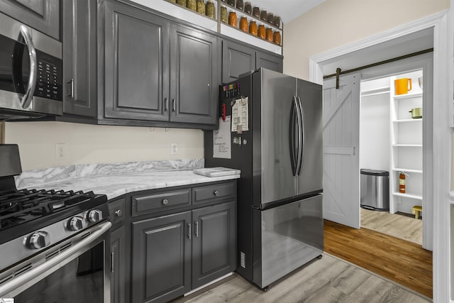 kitchen featuring light stone counters, appliances with stainless steel finishes, a barn door, and light wood-type flooring