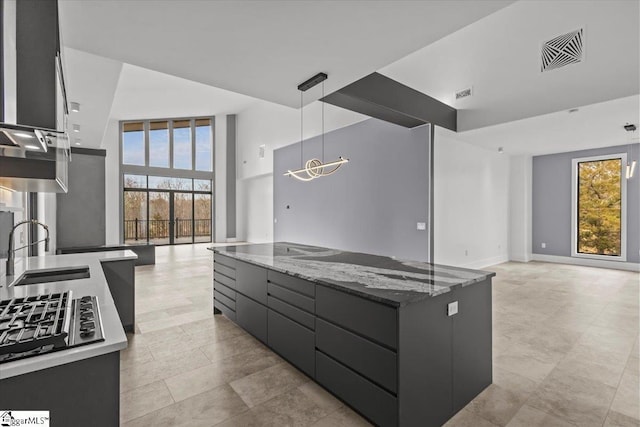 kitchen featuring sink, dark stone countertops, hanging light fixtures, a spacious island, and stainless steel gas cooktop