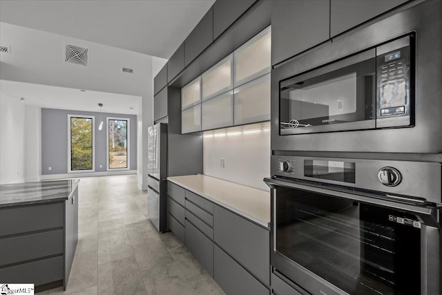 kitchen featuring gray cabinetry, decorative light fixtures, dark stone countertops, and appliances with stainless steel finishes