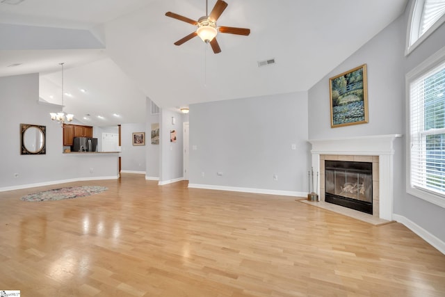 unfurnished living room featuring a tiled fireplace, high vaulted ceiling, ceiling fan with notable chandelier, and light hardwood / wood-style floors